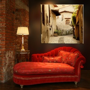 obraz z uliczką w zmysłowej aranżacji salonu z charakterystyczną czerwoną sofą